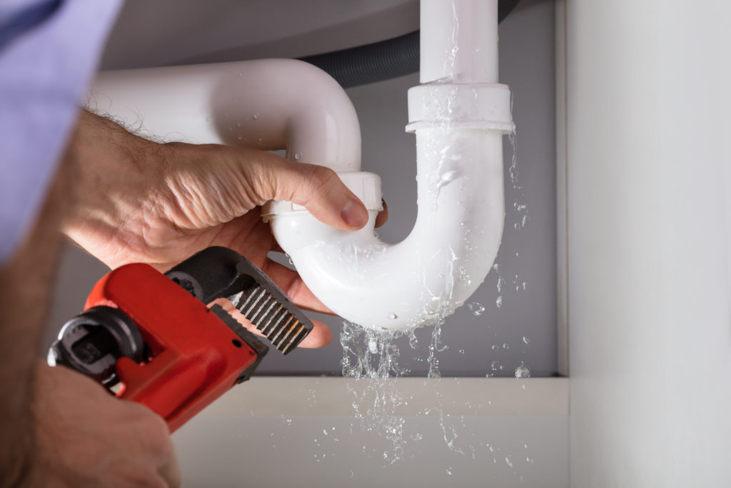 plumber fixing a drain under a sink with red wrench